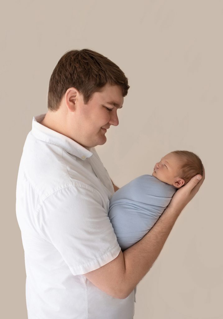 Proud new dad holds baby boy wrapped in pale blue for their first man to man talk