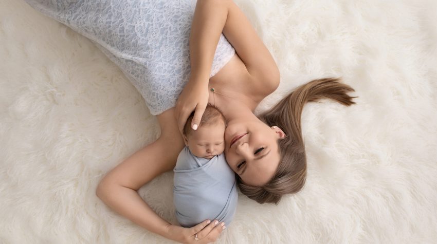 Newborn photography beauty photo baby cuddled by gorgeous new mom dressed in pale blue lace on white fur rug