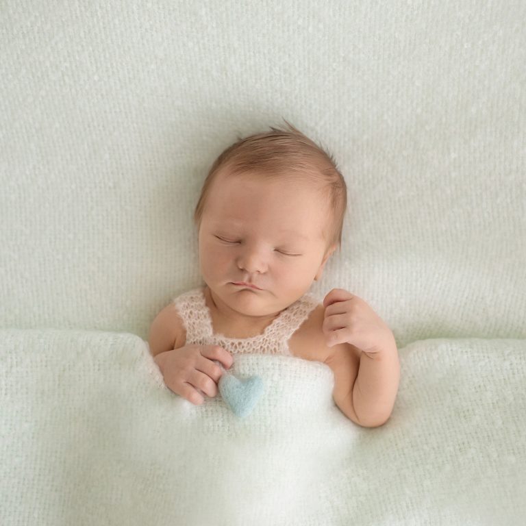 Newborn photography baby boy sleeps tucked into pale mint blanket with green felt heart