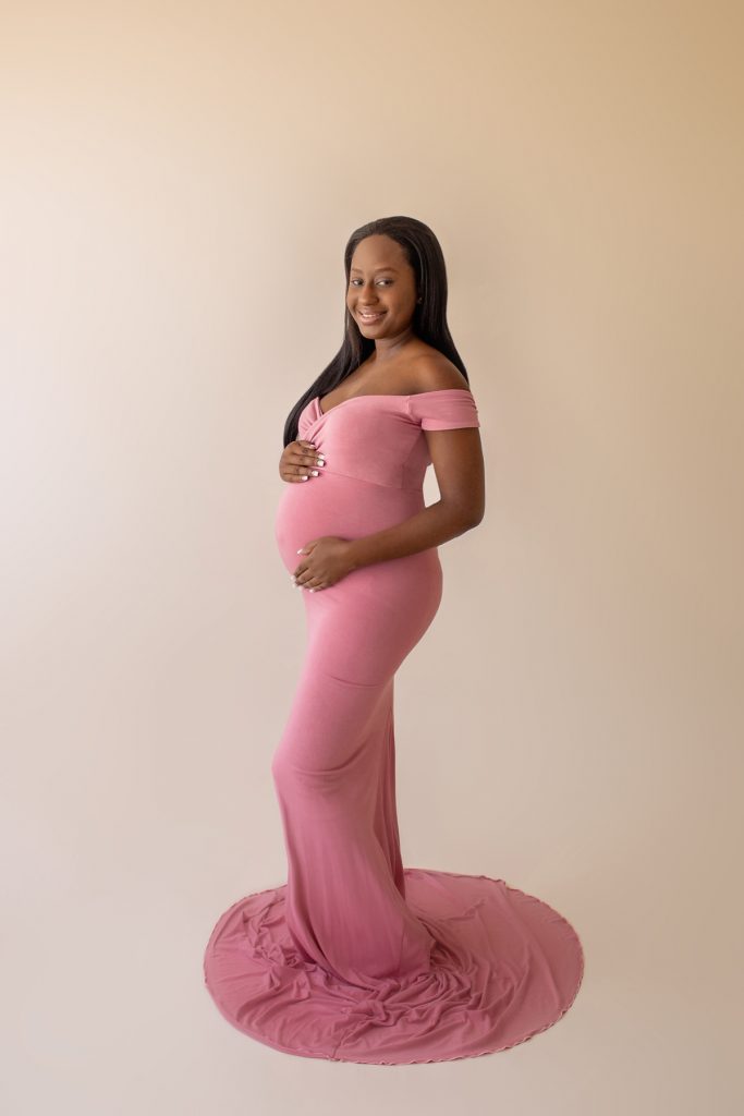 christine deep pink maternity gown expectant mama stands profile holding baby bump looks at camera