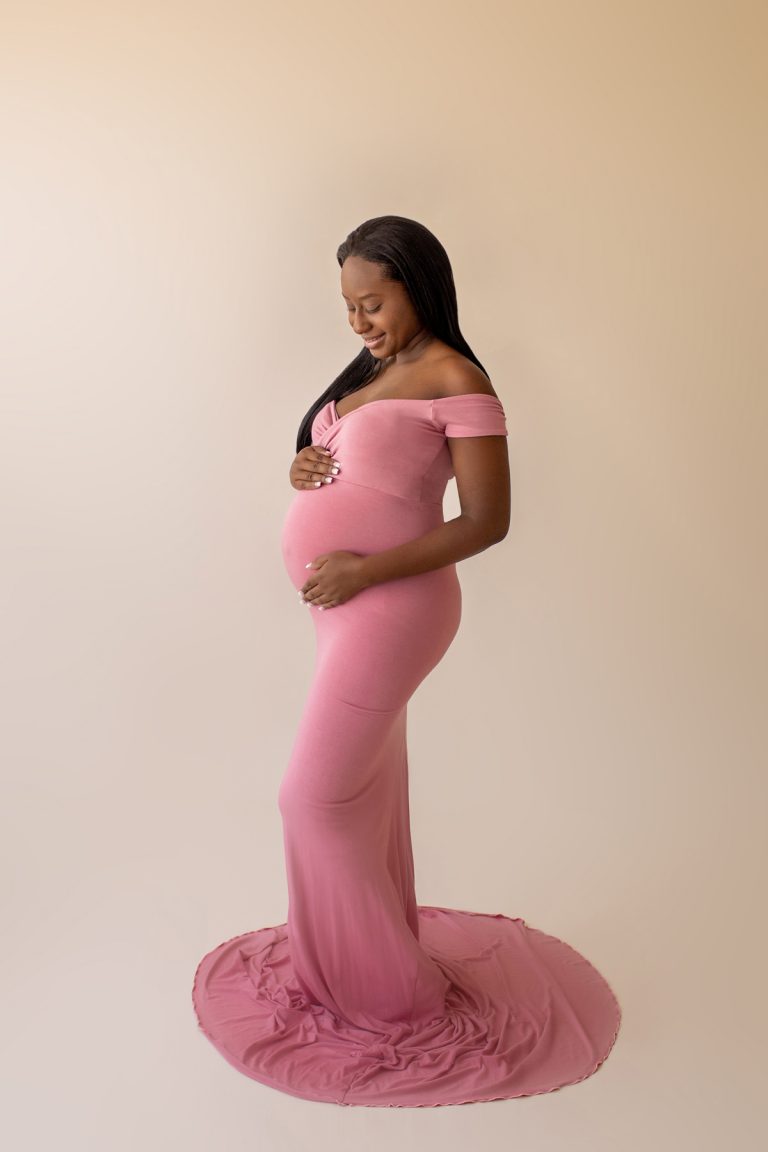 christine deep pink maternity gown expectant mama stands profile admiring baby bump