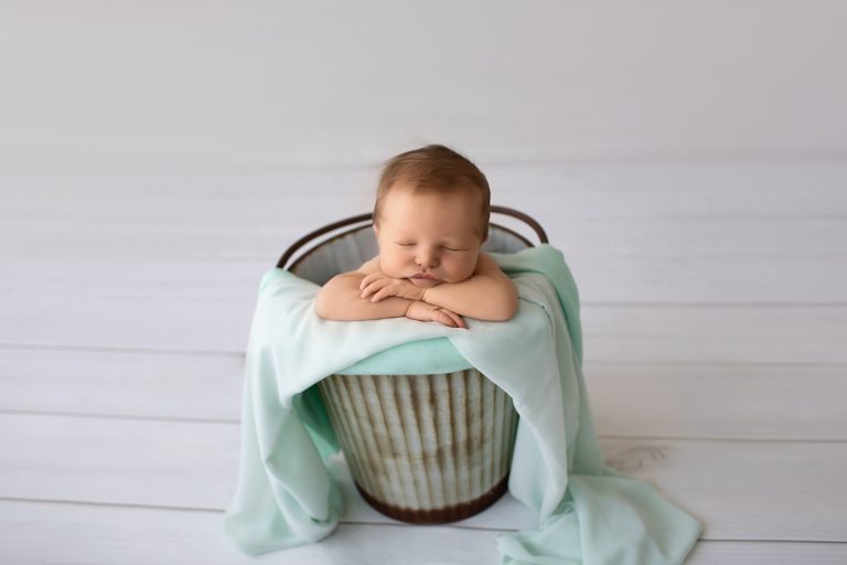 Newborn photography baby boy poses in metal bucket with mint green blanket on grey floor Gainesville FL