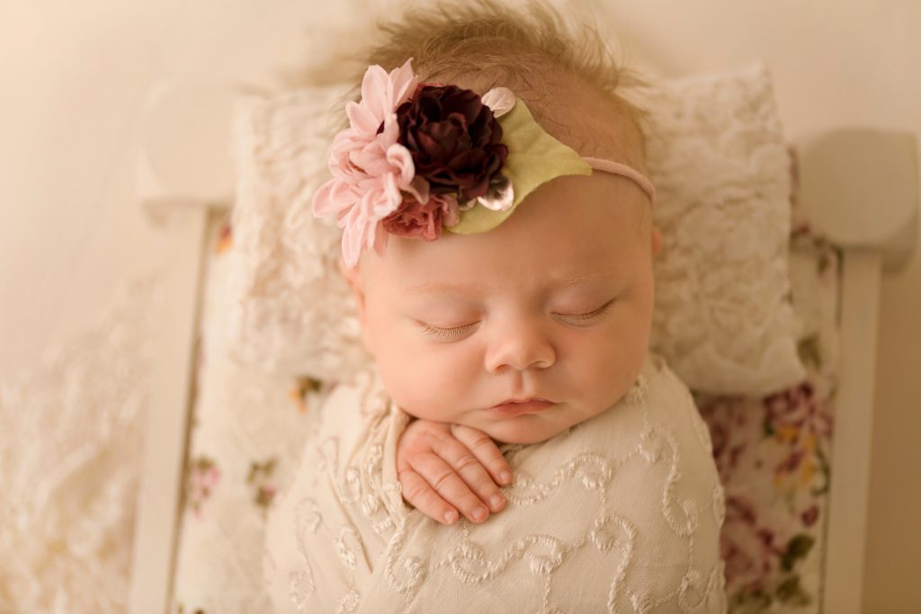 mini newborn photo session girl in ivory lace on floral bed floral headtie