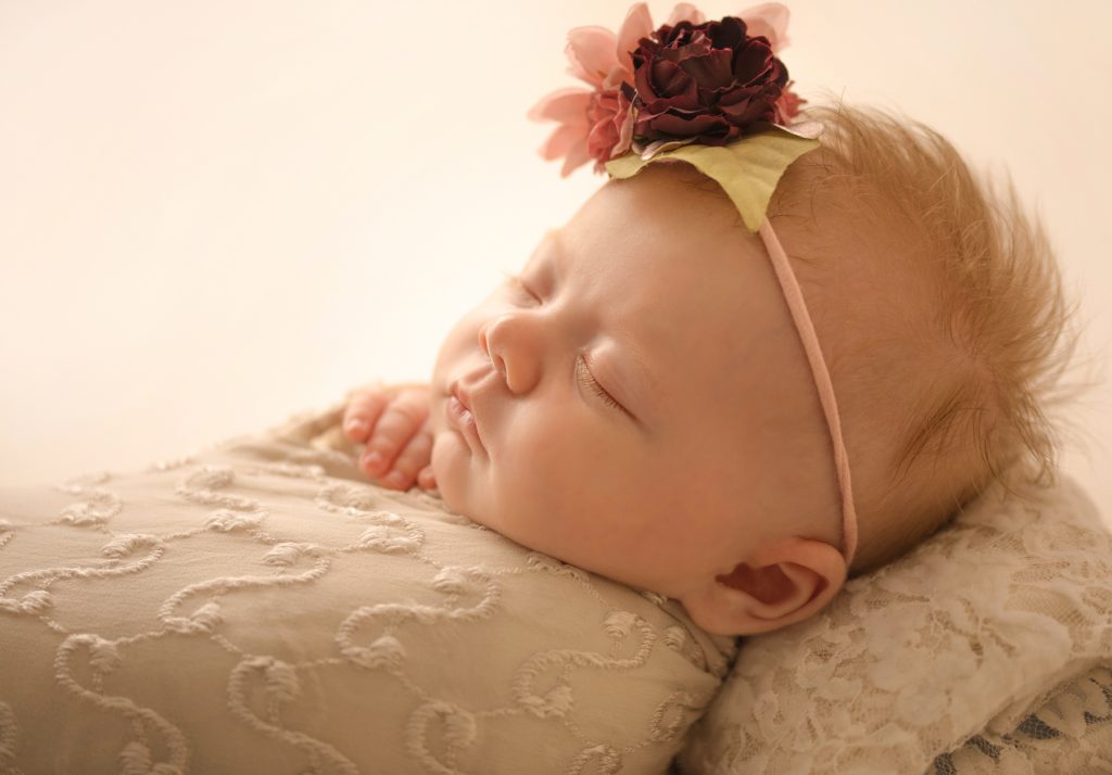 mini newborn photo session girl close up backlit gorgeous eyelashes tiny baby fingers ivory lace on floral bed floral headtie Gainesville FL