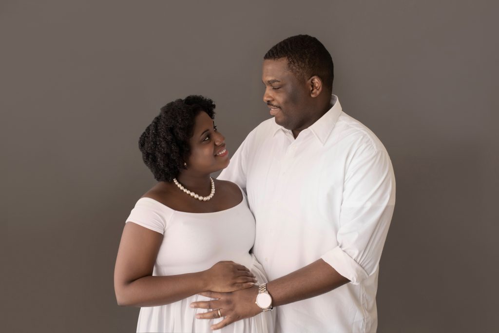 pregnant mom and dad pose look at each other dressed in white holding beautiful baby bump Gainesville FL