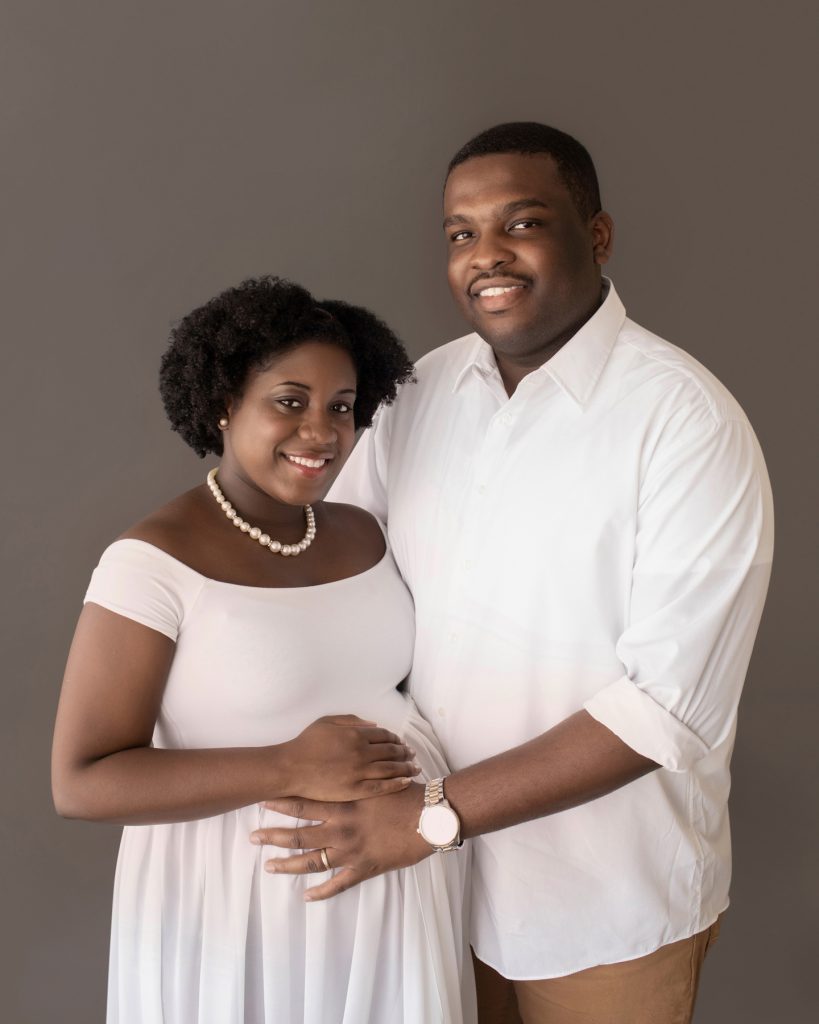 pregnant mom and dad pose smile dressed in white holding beautiful baby bump