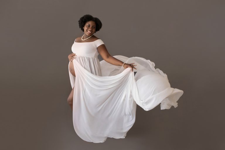 maternity portrait mom wears white chiffon toss gown against grey Gainesville FL