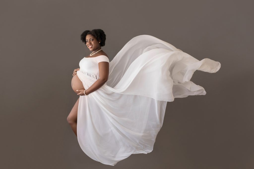 maternity portrait mom poses profile wears white chiffon toss gown against grey Gainesville FL