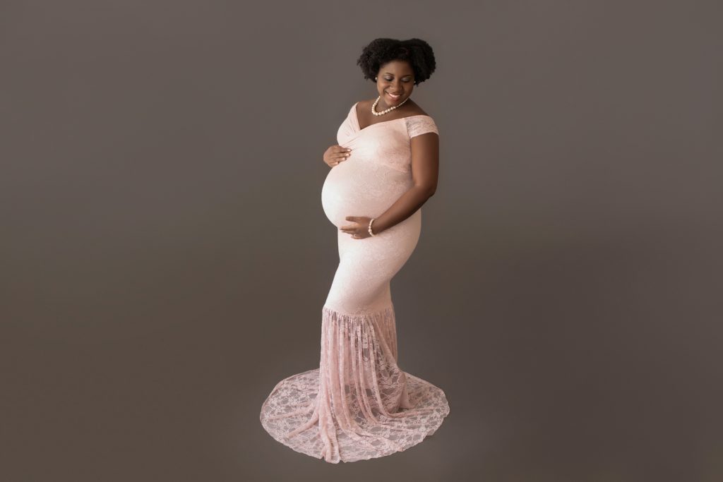 pregnant mom in pink lace mermaid maternity gown decked in pearls hands encircling beautiful baby bump gazing down at belly Gainesville FL