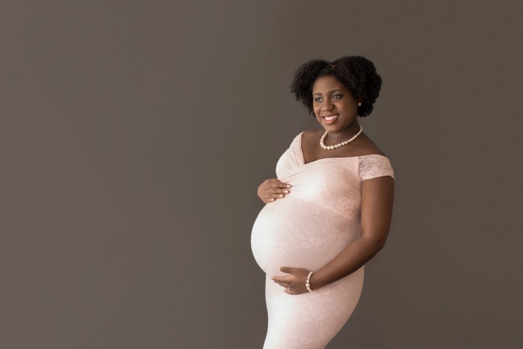 pale pink lace mermaid maternity gown decked in pearls pregnant mom hands encircling beautiful baby bump gazes out window