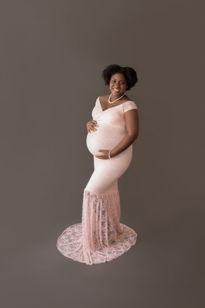 pink lace mermaid maternity gown decked in pearls pregnant mom hands encircling beautiful baby bump smiles at camera