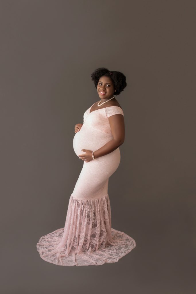 pale pink lace mermaid maternity gown decked in pearls pregnant mom hands encircling beautiful baby bump profile smiles at camera