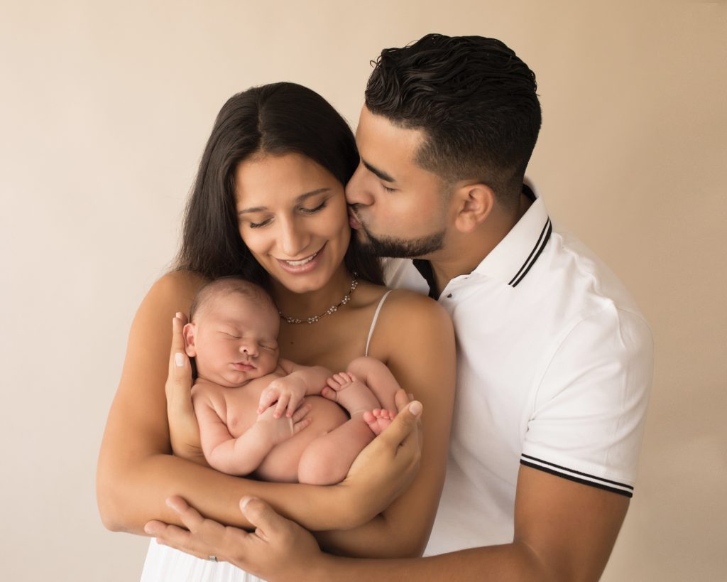 Smiling new mom and dad cuddle baby boy dad kisses mom Gainesville FL newborn mini photo session