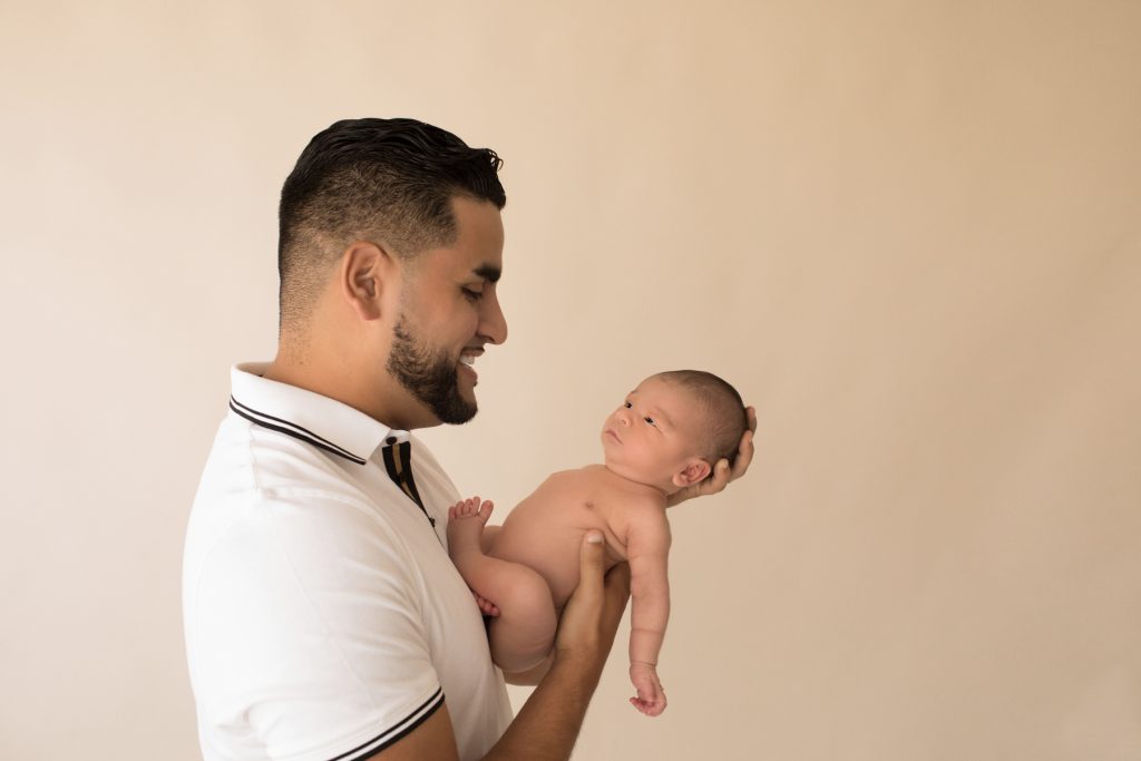 Proud dad holds naked newborn eyes open looking at father Gainesville FL