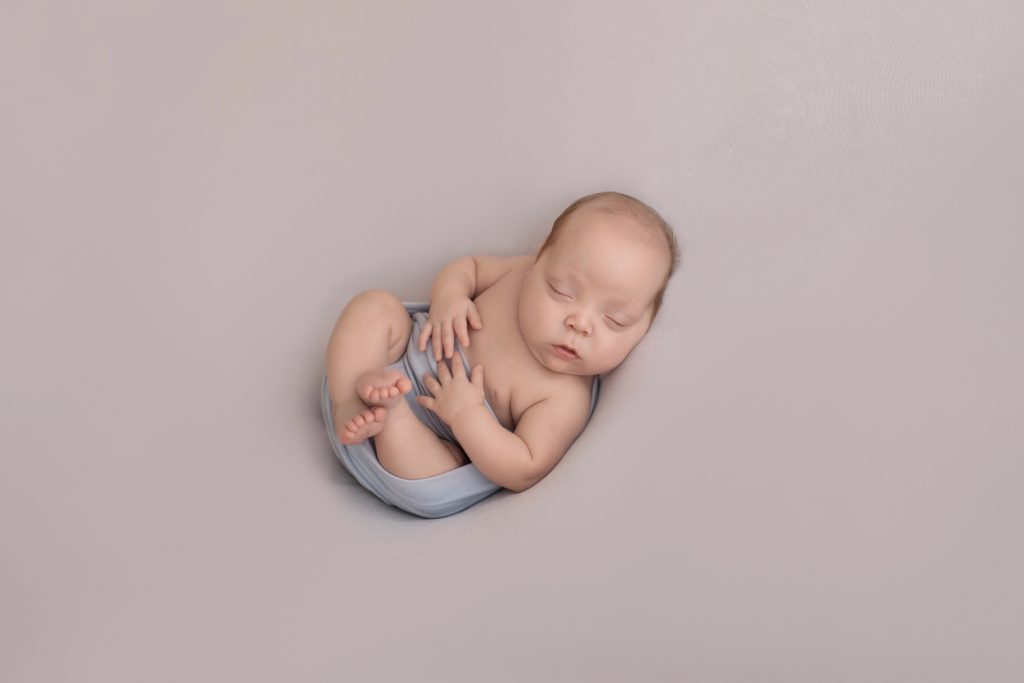 baby in pale blue wrap facing camera tiny baby fingers and toes delicate face baby details Gainesville FL newborn photography