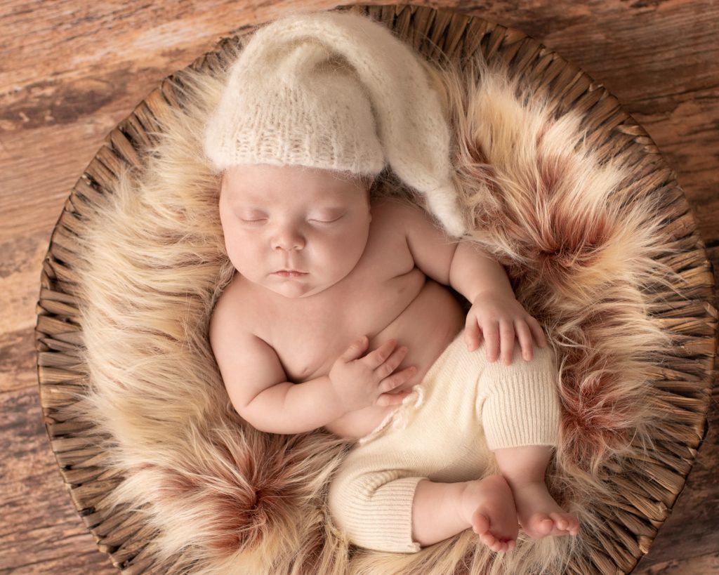 baby boy in fur basket on wood floor cream sleepy hat and pants Gainesville FL newborn photos